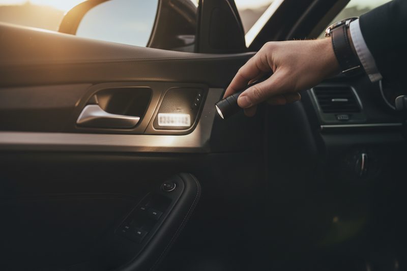 Hand mit Taschenlampe an der geöffneten Fahrertür eines Autos